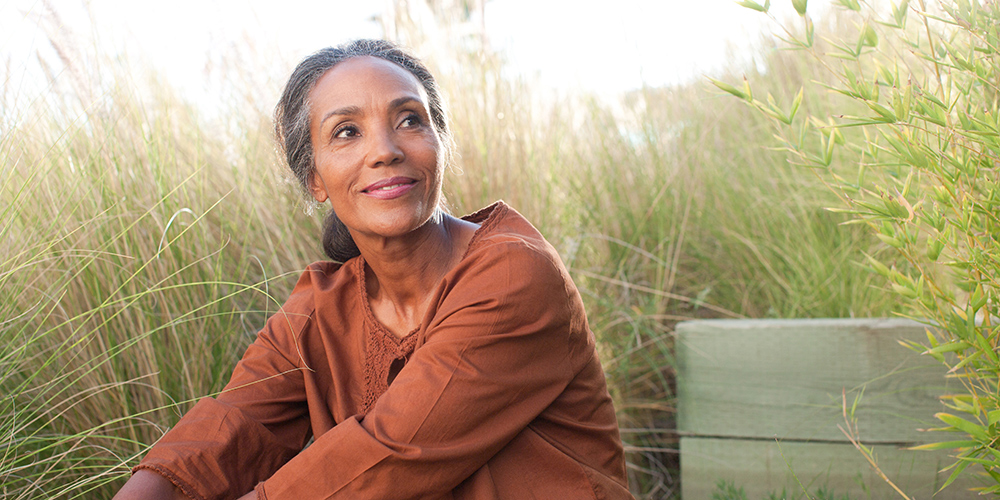Een serene oudere vrouw zit in een zonnig veld, omringd door hoog gras Een serene oudere vrouw zit in een zonnig veld, omringd door hoog gras